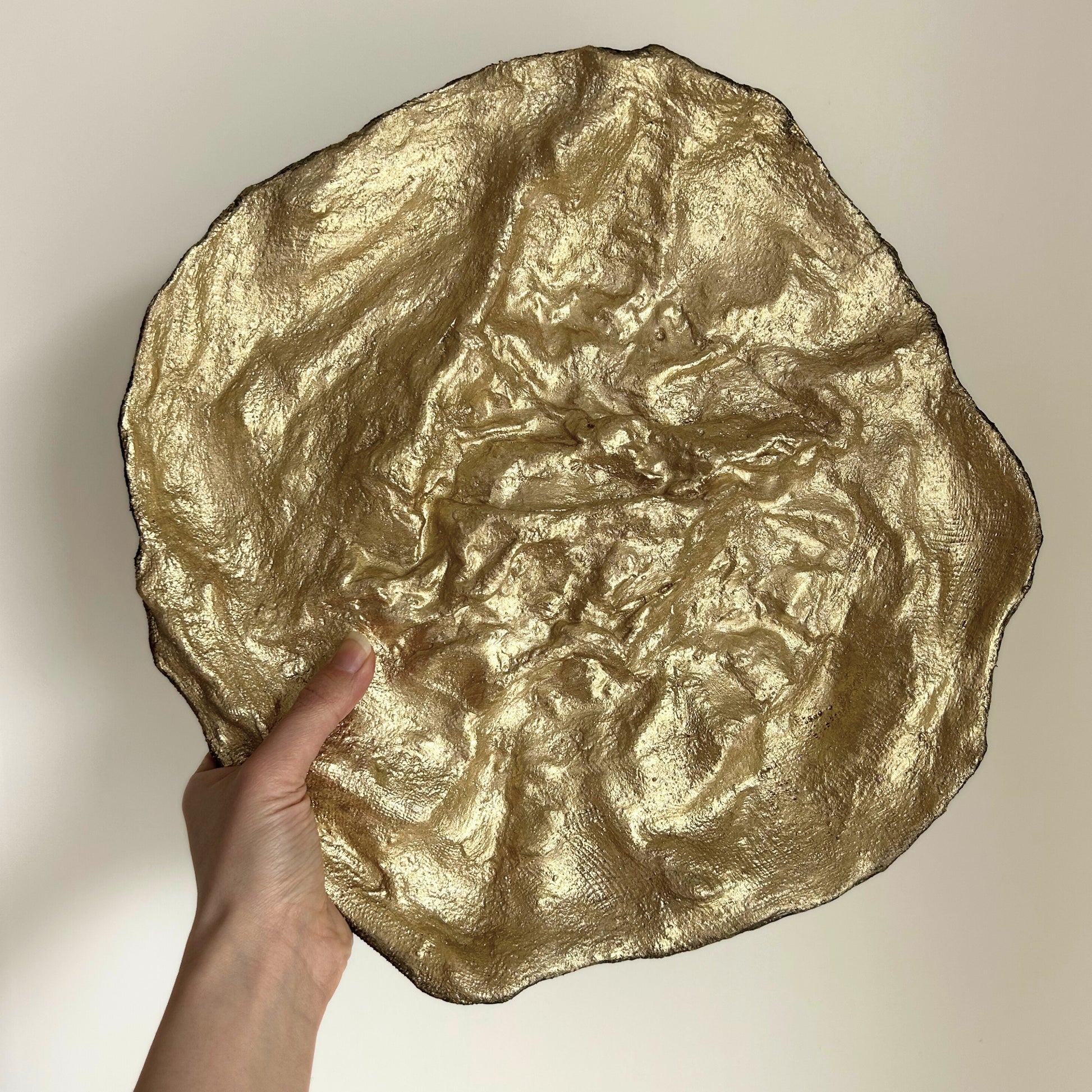 Sculptural gold bowl held in hand, showing asymmetrical shape
