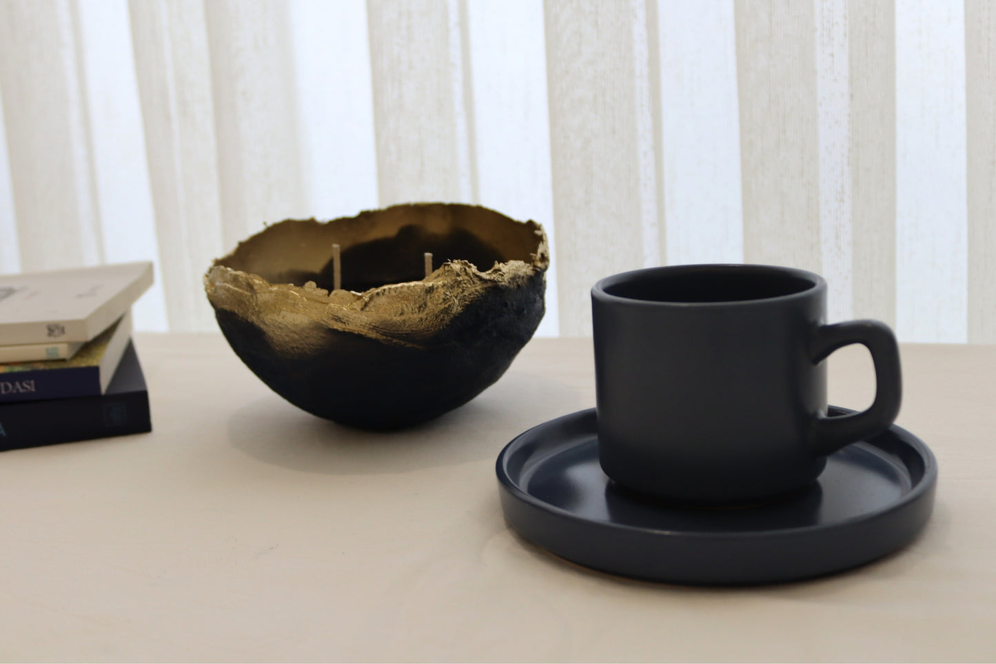 Navy gold candle bowl styled with dark ceramic cup and stacked books on a light surface.
