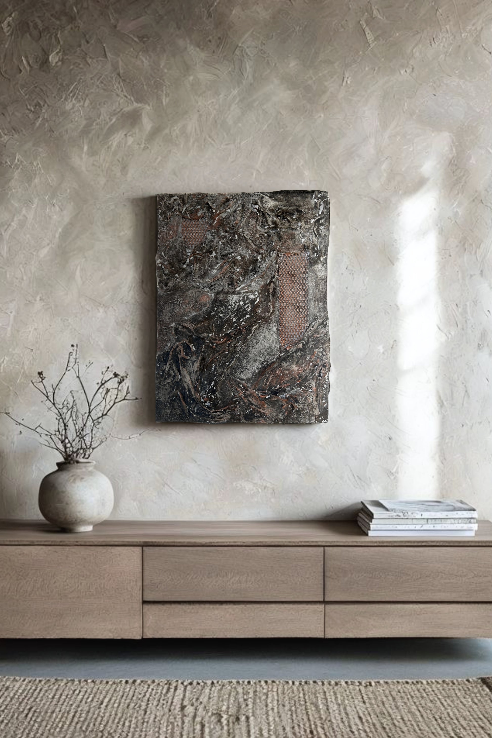 Handmade abstract wall art with black, copper, and earthy textures, displayed on a rustic Japandi-style wall in a modern neutral-toned interior. The artwork is mounted above a wooden console with minimal natural decor, showcasing its raw surface and sculptural relief details.