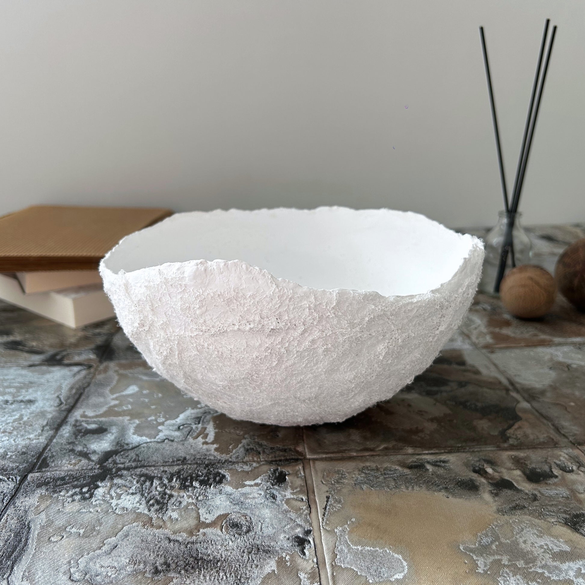 White paper mache bowl placed on a minimalist concrete surface with incense decor in the background