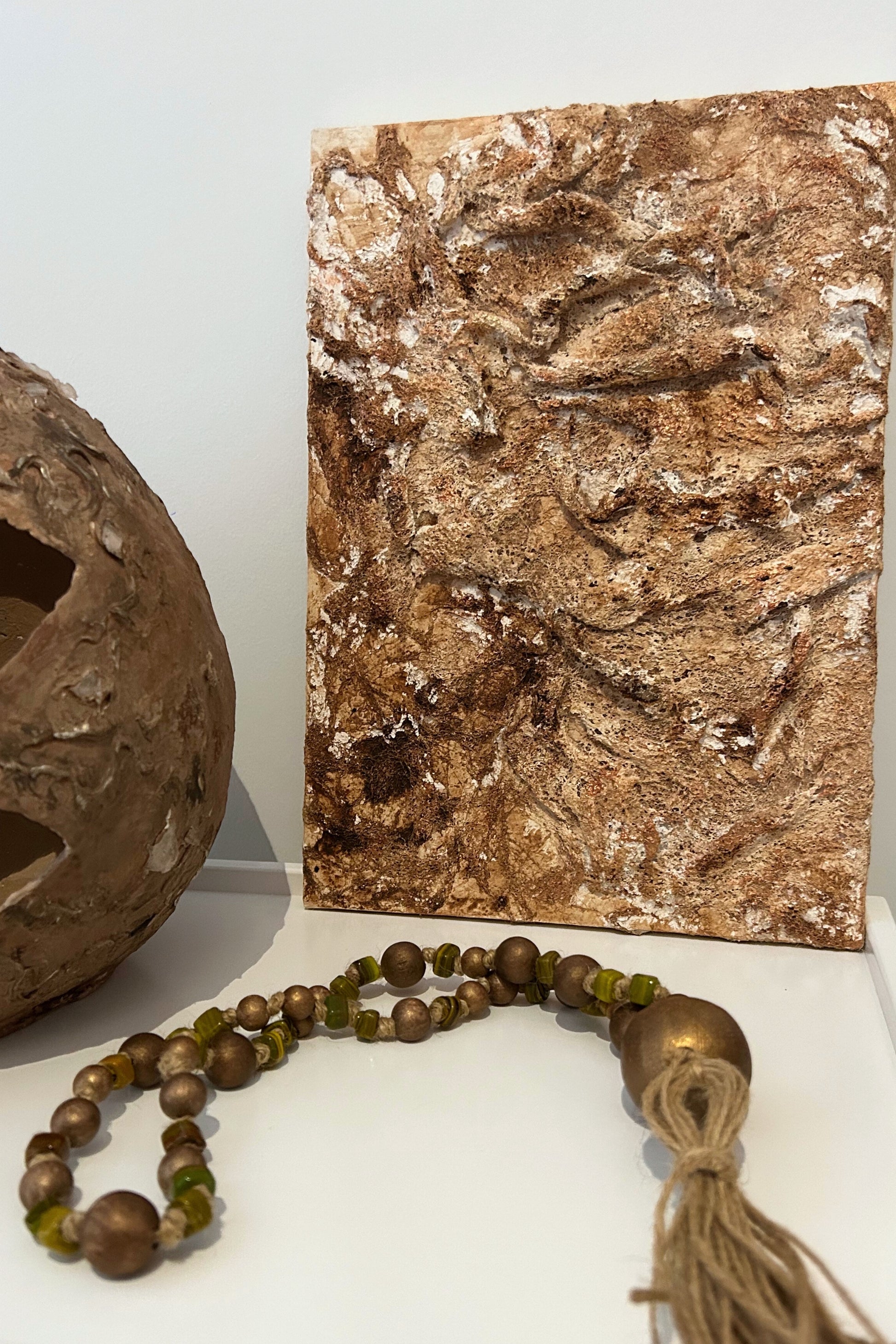 Rustic wall art styled next to natural ceramics and wooden beads in a Japandi setting.