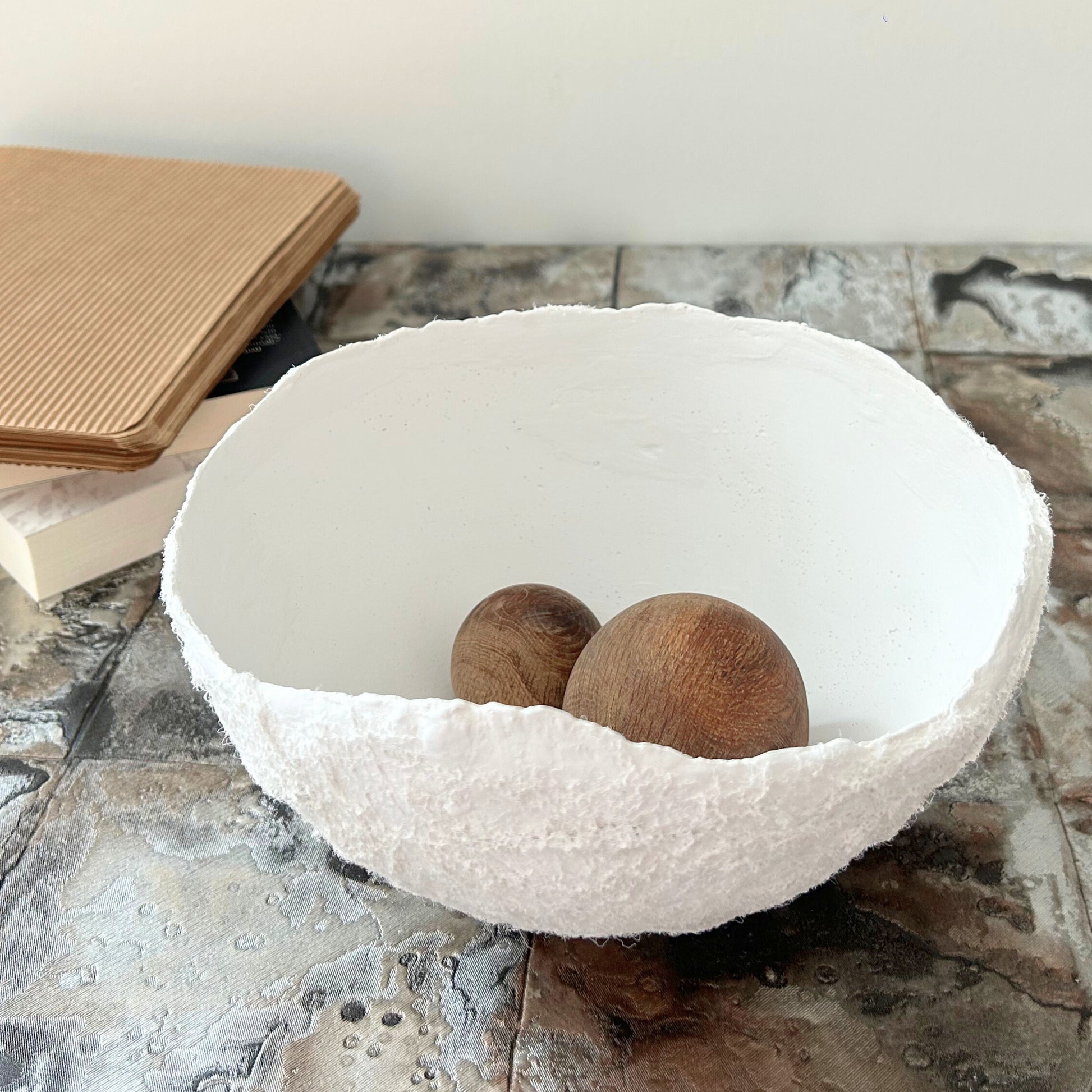 White decorative bowl with wooden balls styled on a stone-textured surface, showcasing rustic function