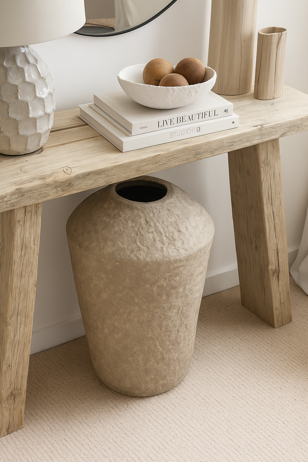 Set of three natural wooden spheres placed in a white textured bowl atop a rustic wooden console table with stacked neutral books and minimalist boho accents.