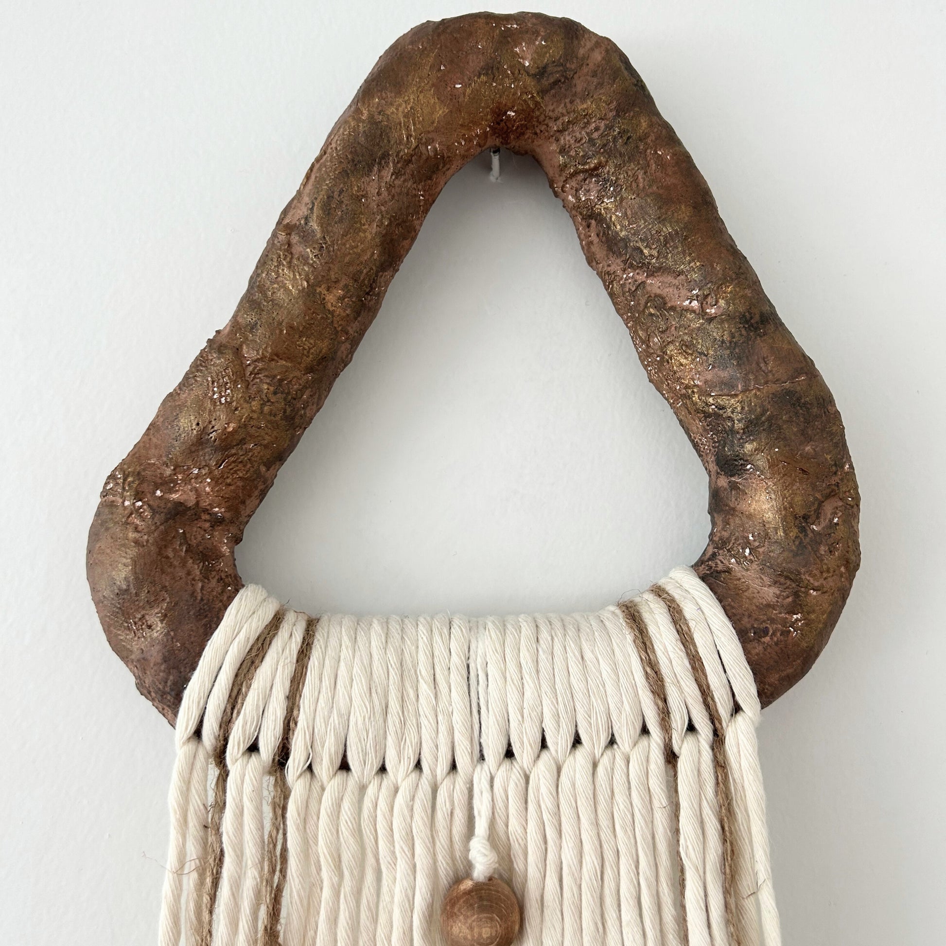 Sculptural triangle plaster hanger in bronze tones, holding a minimalist yarn wall hanging.